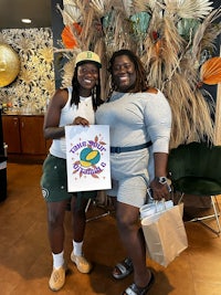 two women posing for a photo in front of a tropical decor